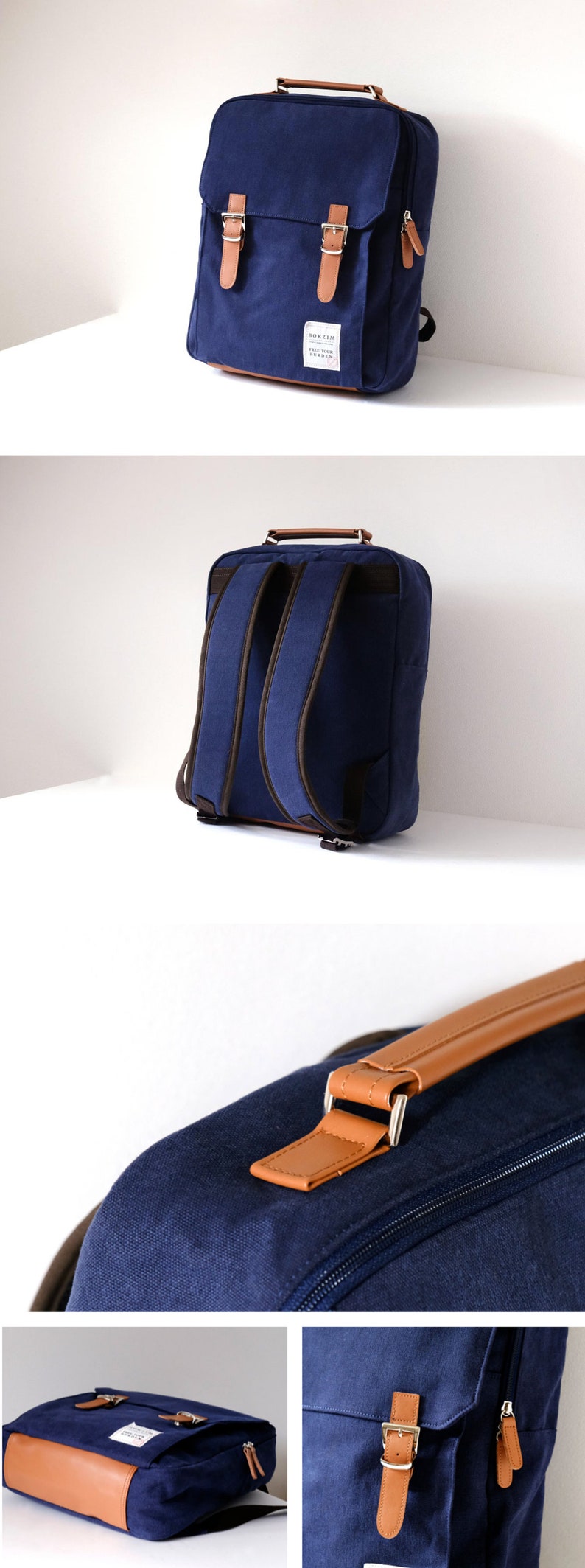 May include: A navy blue canvas backpack with brown leather accents and buckles. The backpack has a top handle and a zippered front pocket. The brand name "ROKZIM" is printed on a white label on the front of the bag.