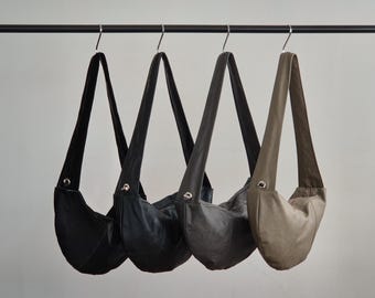 May include: Three leather tote bags hanging on a rack. The bags are in black, gray, and brown.