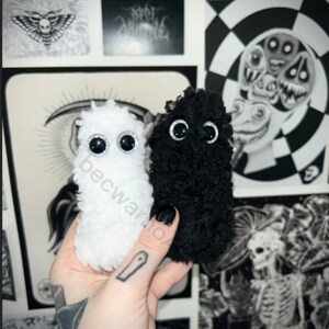May include: Two small plush toys, one white and one black, with large black eyes. Both toys have a fuzzy texture.