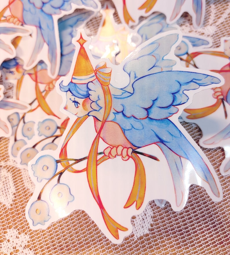 May include: A blue bird with a yellow crown and a yellow ribbon is perched on a branch with white flowers. The bird has a pink body and blue wings. The background is white.
