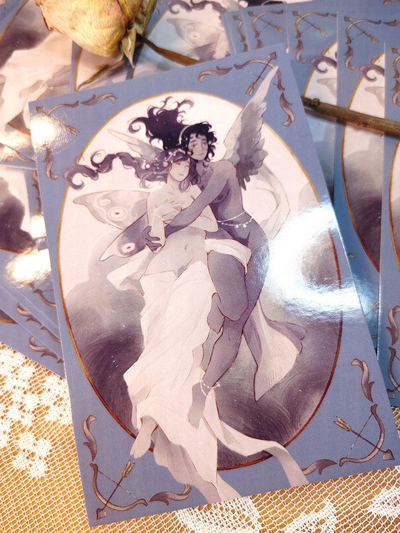 May include: A blue and gold postcard featuring a watercolor illustration of two figures embracing. The figure on the left has butterfly wings and the figure on the right has angel wings. The background is a soft blue with a gold border.