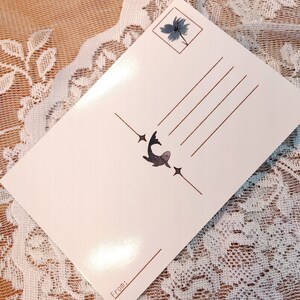 May include: A white postcard with a brown border and a small illustration of a fish with stars on either side. The postcard has a space for a message and a "From:" section at the bottom.