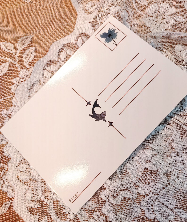 May include: A white postcard with a brown border and a small illustration of a fish with stars on either side. The postcard has a space for a message and a "From:" section at the bottom.