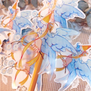 May include: A set of four clear stickers featuring a whimsical illustration of a blue bird with wings, wearing a party hat and holding a yellow ribbon. The bird is surrounded by blue flowers.