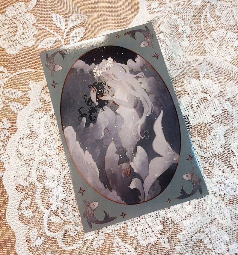 May include: A watercolor illustration of two mermaids with long flowing hair, one with dark hair and the other with white hair, embracing in a swirling sea of blue and white. The mermaids are surrounded by small fish and stars.