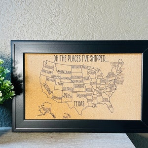 May include: A corkboard with a black frame and a map of the United States. The map is labeled with the names of each state. The text "Oh the places I've shipped..." is at the top of the corkboard.