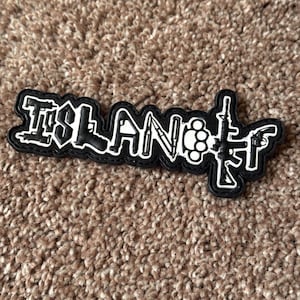 May include: Black and white patch with the word "ISLAND" and weapon illustrations. The patch features a black background with white outlines and details, including a knife, brass knuckles, and firearms.