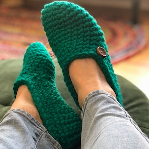May include: A pair of green crocheted slippers with a button on the top of each slipper.