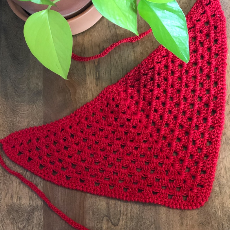 May include: A red crocheted triangular scarf with a fringe. The scarf is made with a simple stitch pattern and has a delicate, lacy look.