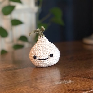 May include: A white crocheted garlic with a green stem and a smiling face.