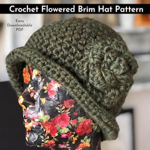May include: A green crochet hat with a flower design on the side. The hat is on a mannequin head with a floral pattern.
