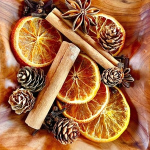 May include: A wooden bowl filled with dried orange slices, cinnamon sticks, star anise, pine cones, and cloves. The bowl is a natural wood color and the ingredients are arranged in a decorative pattern.
