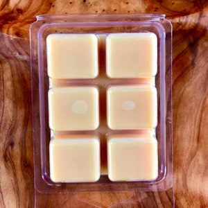 May include: A clear plastic tray with six square wax melts. The wax melts are a light yellow color.