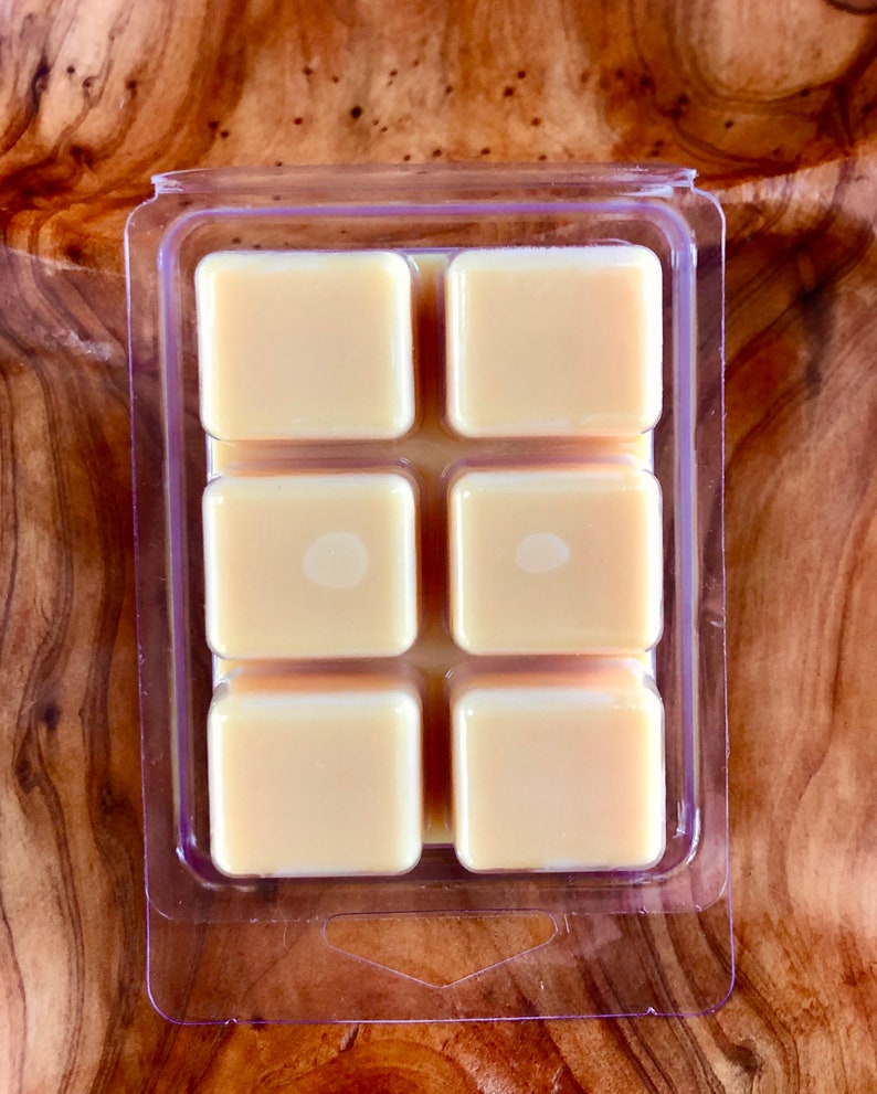 May include: A clear plastic tray with six square wax melts. The wax melts are a light yellow color.