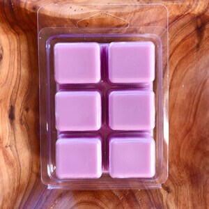 May include: Six square wax melts in a clear plastic clamshell packaging. The wax melts are a light purple color.