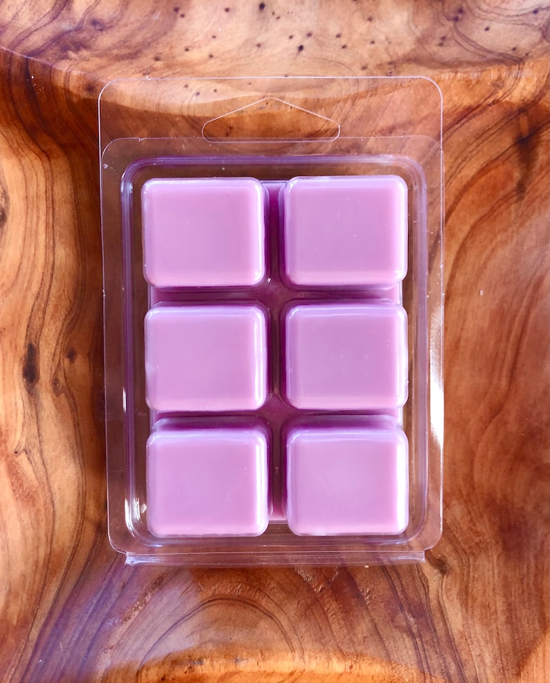 May include: Six square wax melts in a clear plastic clamshell packaging. The wax melts are a light purple color.