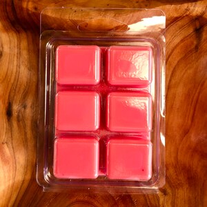May include: A clear plastic package containing six pink wax melts. The wax melts are arranged in a 2x3 grid.
