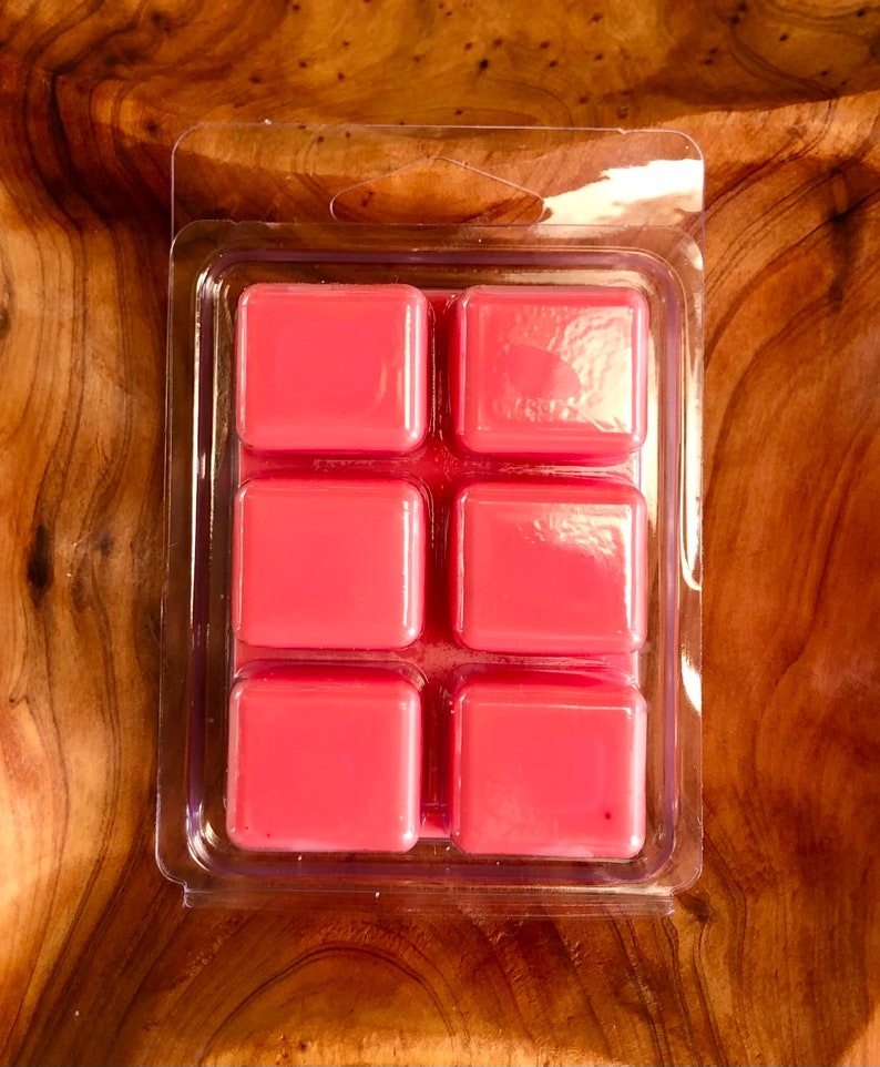 May include: A clear plastic package containing six pink wax melts. The wax melts are arranged in a 2x3 grid.