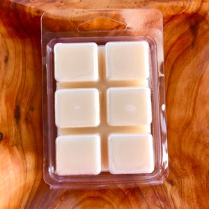 May include: A clear plastic tray with six square wax melts. The wax melts are a light beige color.