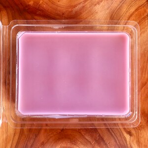 May include: A clear plastic container with a light purple wax melt inside.