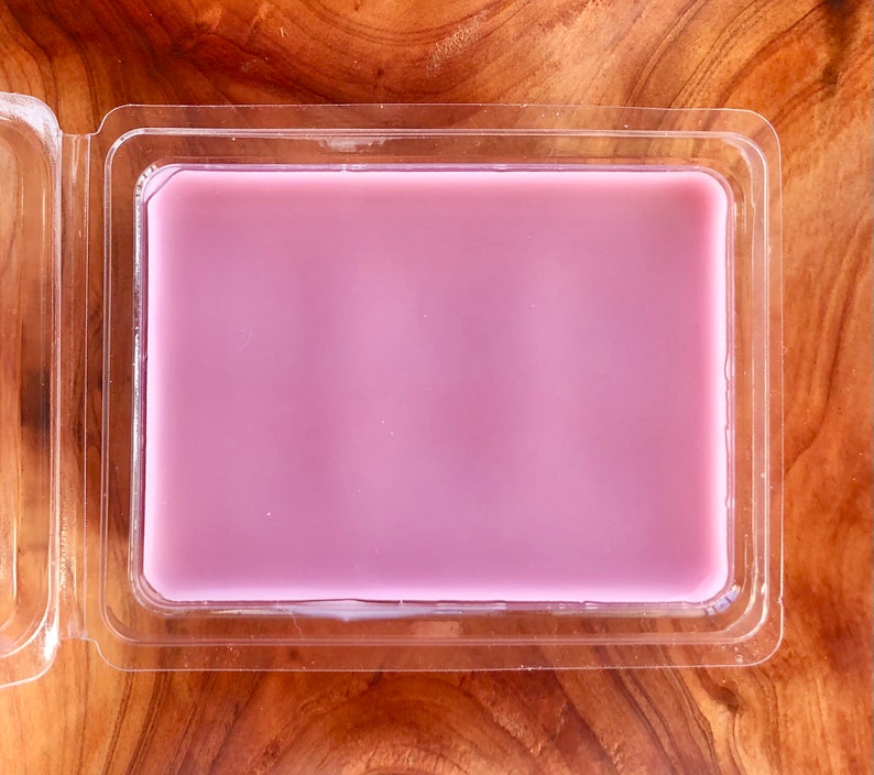 May include: A clear plastic container with a light purple wax melt inside.