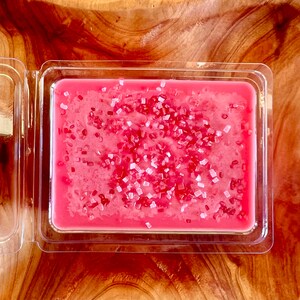 May include: A pink wax melt with white sprinkles in a clear plastic container.