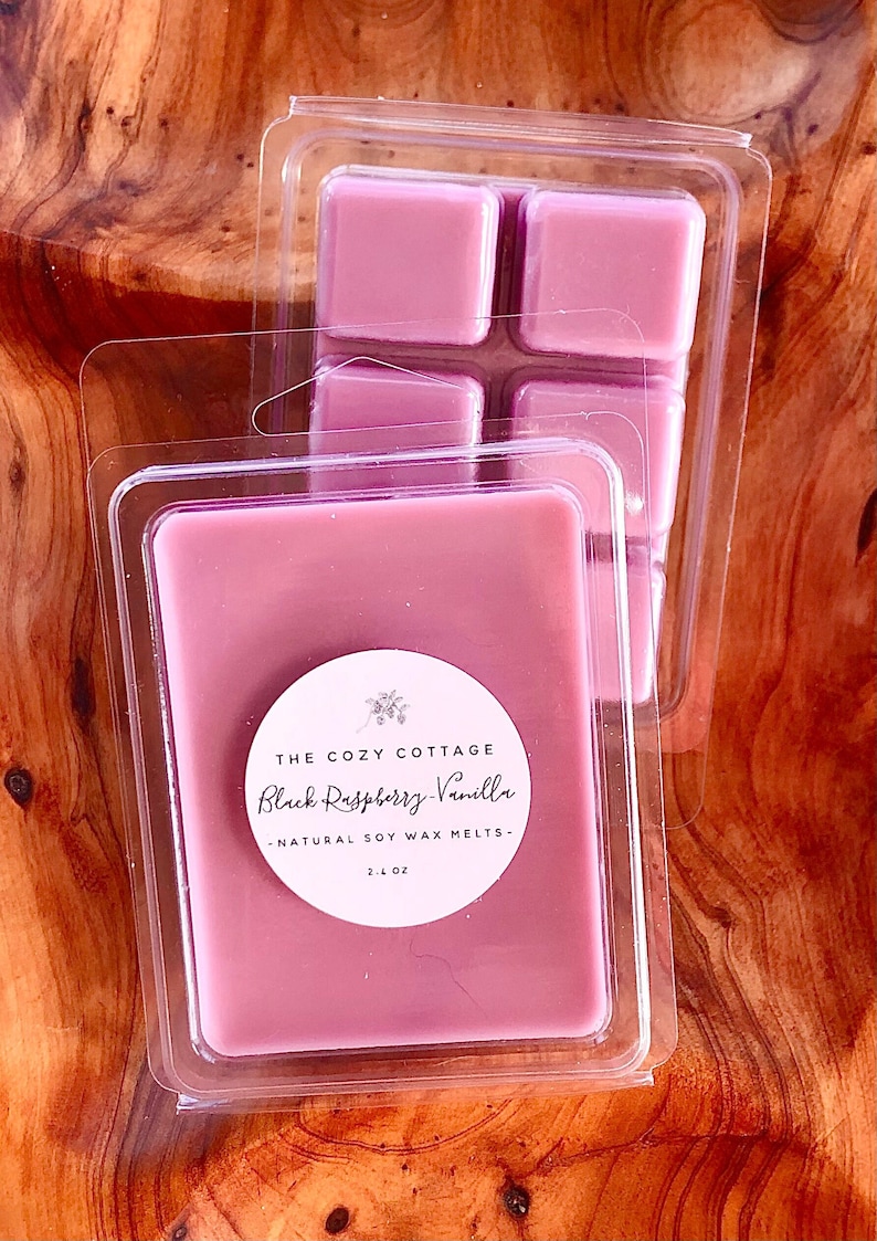 May include: A package of four pink soy wax melts in a clear plastic container. The label reads "The Cozy Cottage Black Raspberry Vanilla - Natural Soy Wax Melts - 2.1 oz."