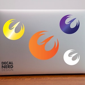 May include: Four Rebel Alliance symbol stickers on a silver laptop. The stickers are in yellow, orange, purple, and white.