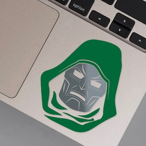 May include: A green and gray vinyl sticker of Doctor Doom's face. The sticker is on a silver laptop.