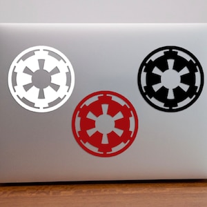 May include: Three Imperial Star Wars logos on a silver laptop. The logos are white, black, and red.