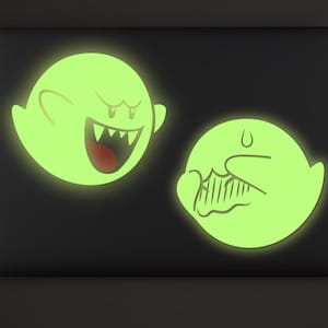 May include: Two glow-in-the-dark vinyl decals on a black laptop surface. One decal shows a laughing ghost with sharp teeth, and the other shows a shy ghost covering its face. The text DECAL NERD DESIGN appears in the top right corner.