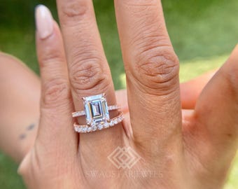 May include: A rose gold ring set featuring a large emerald-cut center stone held by four prongs, paired with a matching band encrusted with small round-cut stones. The metal has a warm pinkish hue, and the stones are clear and faceted.