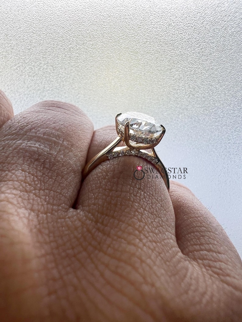 May include: Close-up of a gold ring featuring a large, oval-cut diamond as the centerpiece. The band is also adorned with smaller diamonds. The ring is set against a neutral background, highlighting the sparkle of the gemstones. The ring is a piece of jewelry.