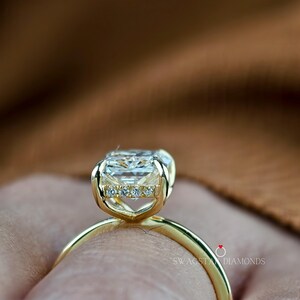 May include: Close-up of a gold ring featuring a large, rectangular-cut diamond. The ring has a delicate band and a setting with smaller accent diamonds. The ring is set against a blurred background.