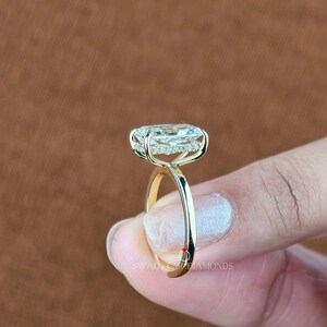 May include: A gold ring with a large, oval-shaped diamond center stone. The diamond is surrounded by a halo of smaller diamonds. The ring band is smooth and polished. The text "SWAG DIAMONDS" is visible on the ring.