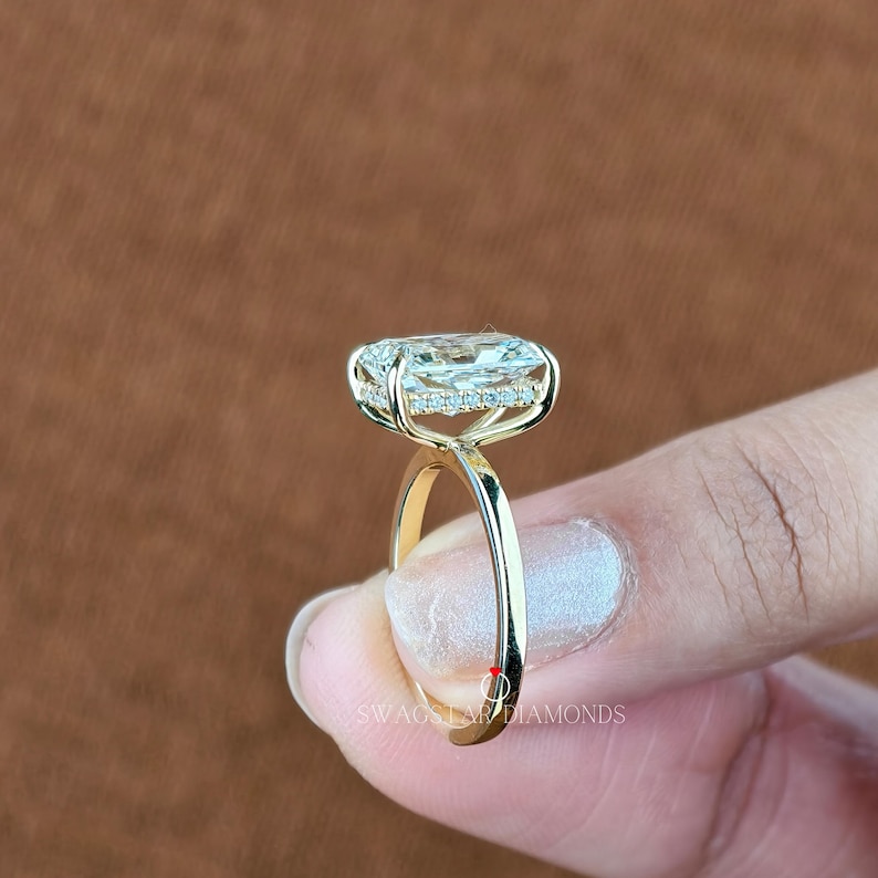 May include: A gold ring with a large, oval-shaped diamond center stone. The diamond is surrounded by a halo of smaller diamonds. The ring band is smooth and polished. The text "SWAG DIAMONDS" is visible on the ring.