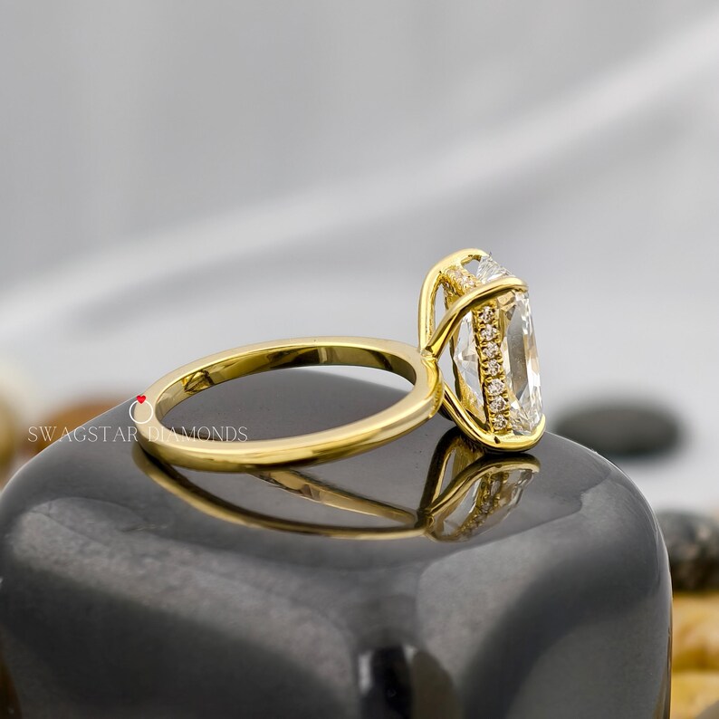 May include: A gold ring with a large, rectangular, clear gemstone. The ring has a delicate band and a halo of smaller stones around the main gem. The brand name "SWAGSTAR DIAMONDS" is visible on the ring's band.