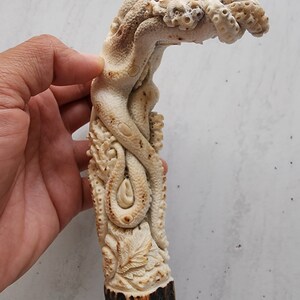 May include: A carved, off-white sculpture of an octopus with detailed tentacles and a textured surface. The base of the sculpture has a dark brown, rough texture. The octopus design is intricately carved, showcasing a unique artistic style.