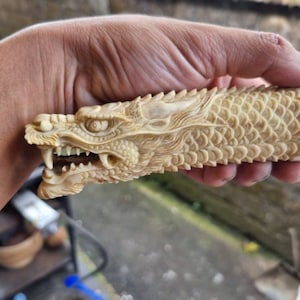 May include: A detailed carving of a dragon's head, with intricate scales and sharp teeth, is crafted from bone. The dragon's head is attached to a bone handle.