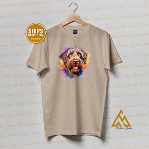 Peut inclure: Un t-shirt beige avec une illustration aquarelle d'un chien brun et blanc avec une touche de peinture violette, bleue et jaune.