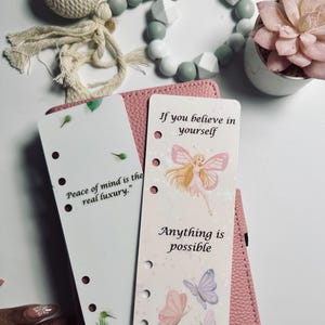 May include: A pink leather planner with two decorative inserts. One insert reads "Peace of mind is the real luxury." The other insert features a fairy illustration and the text "If you believe in yourself, Anything is possible."