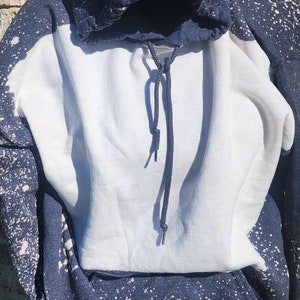 May include: A navy blue hoodie with white splatter paint. The hoodie has a white front panel and a drawstring hood.