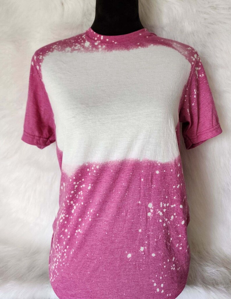 Puede incluir: Una camiseta rosa y blanca con un dise&ntilde;o salpicado de lej&iacute;a. La camiseta tiene cuello redondo y mangas cortas.