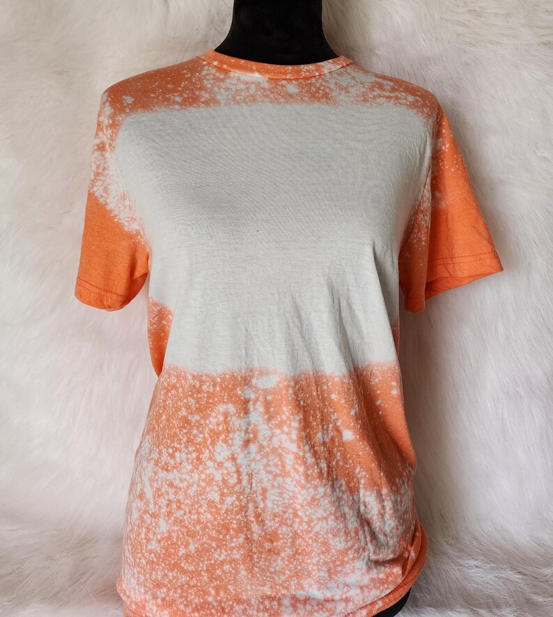 Puede incluir: Una camiseta tie-dye blanca y naranja con un dise&ntilde;o salpicado de lej&iacute;a.