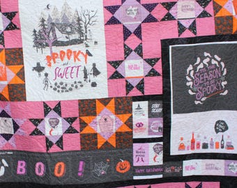 Könnte beinhalten: Ein Halloween-Quilt mit verschiedenen Mustern und Texten. Der Quilt zeigt rosa, schwarze, orangefarbene und weiße Quadrate mit Sätzen wie "Spooky and Sweet" und "Tis the Season to be Spooky". Er enthält auch Bilder eines Spukhauses, Geister und Kürbisse.