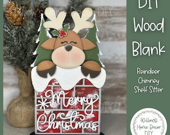 Puede incluir: Un adorno navideño de madera con un reno asomándose por encima de una chimenea de ladrillo. La chimenea tiene las palabras "Merry Christmas" en escritura blanca. El reno tiene cuernos y está flanqueado por árboles verdes. La base es negra.