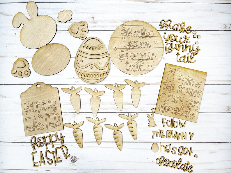 May include: A set of unfinished wooden Easter craft supplies, including bunny shapes, carrots, eggs, and signs with the text "Shake your bunny tail" and "Follow the bunny, he's got chocolate".
