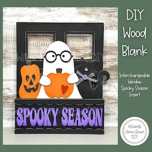 May include: A black wooden window frame with a spooky season insert. The insert features a ghost holding a pumpkin, a black cat, and a pumpkin with a jack-o-lantern face. The window frame has the words "Spooky Season" written in purple letters.