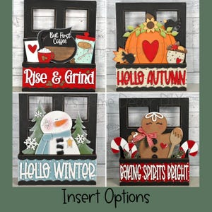 May include: Four wooden window frame signs with interchangeable inserts. The signs feature different seasonal themes: "But First Coffee" with a coffee cup and mug, "Rise & Grind", "Hello Autumn" with a pumpkin and leaves, "Hello Winter" with a snowman, and "Baking Spirits Bright" with a gingerbread man.