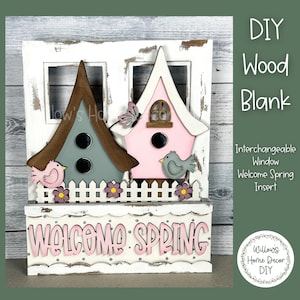 May include: DIY wood blank with interchangeable window insert featuring a welcome spring sign, two birdhouses, and a picket fence. The birdhouses are painted pink and blue with brown roofs. The sign is white with pink lettering and polka dots. The birdhouses have small bird cutouts and a butterfly cutout.